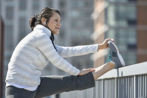 Hispanic woman stretching leg in city