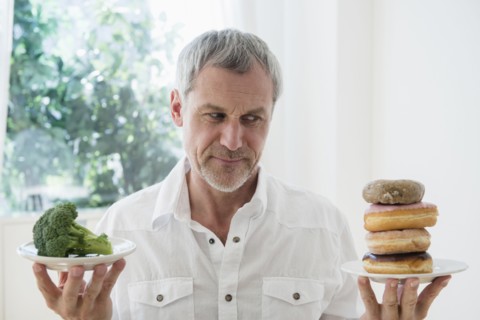 Older Caucasian man choosing between broccoli and donuts