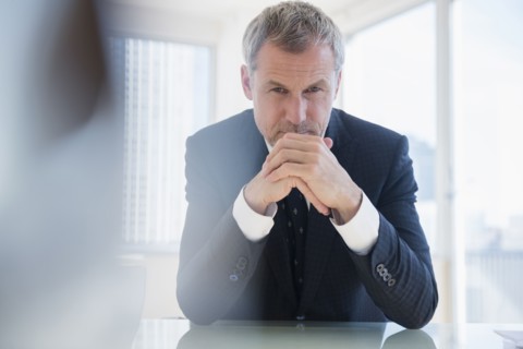 Serious older Caucasian businessman leaning on desk