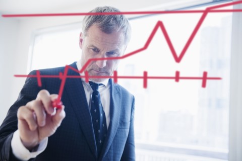 Older Caucasian businessman drawing chart on glass wall