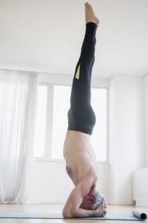 Older Caucasian man doing headstand on exercise mat