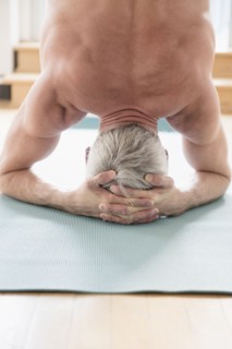 Older Caucasian man doing headstand on exercise mat