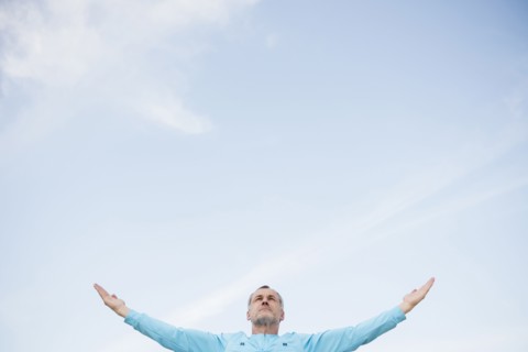 Older Caucasian man with arms outstretched against blue sky