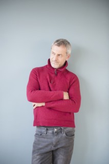 Older Caucasian man wearing sweater leaning on wall