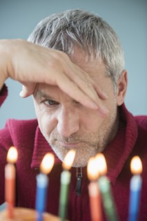 Older Caucasian man frowning at birthday cake