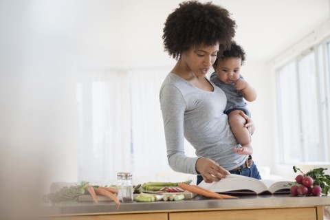 Mother reading cookbook while holding baby son