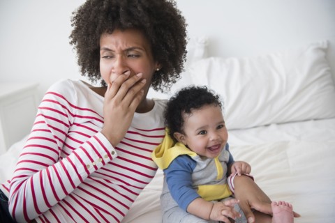 Mother yawning on bed holding baby son