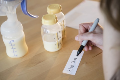 Caucasian woman writing date and volume for breast milk bottles