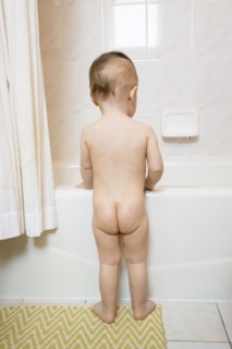 Naked Caucasian baby girl standing at bathtub