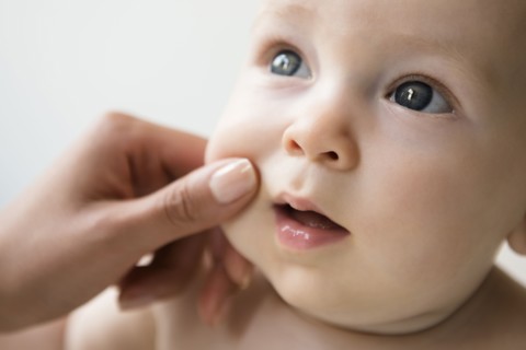 Hand of mother pinching cheek of baby son