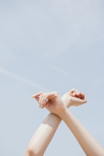 Hispanic woman crossing arms at wrist under blue sky