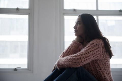 Hispanic woman wearing pink sweater and jeans near window