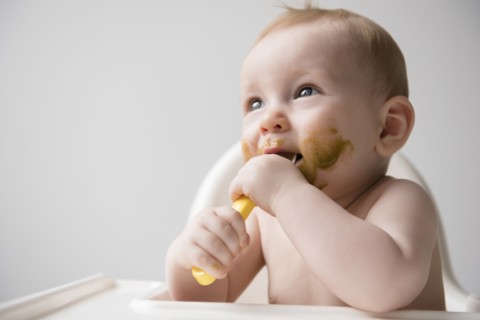 Messy Caucasian baby boy eating from spoon in high chair