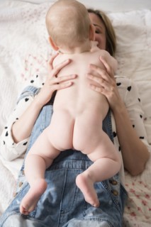 Caucasian mother laying on bed holding naked baby son