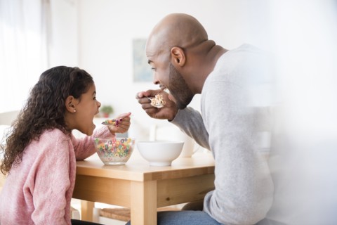 Father and daughter eating cereal at table