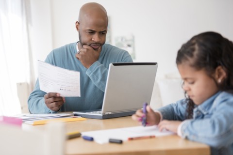 Daughter coloring with crayons while father uses laptop