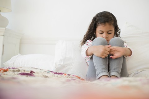 Unhappy Mixed Race girl sitting on bed