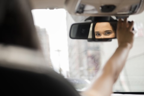 Mixed Race woman adjusting rear-view mirror in car