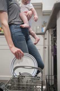 Caucasian mother holding baby son holding plate in dishwasher