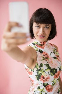 Hispanic woman wearing floral dress posing for cell phone selfie