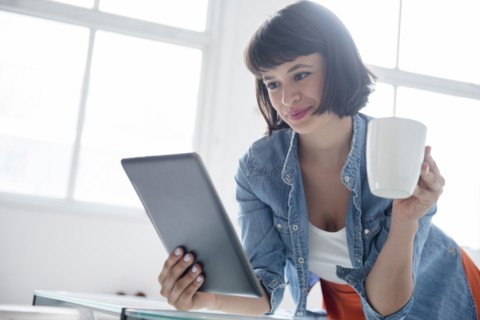 Hispanic woman drinking coffee and reading digital tablet