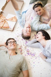 Caucasian friends laying on floor with pizza and confetti