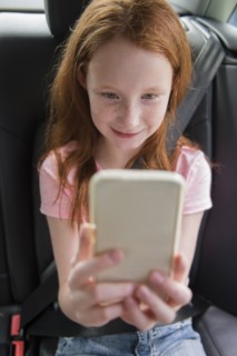 Smiling Caucasian girl texting on cell phone in car