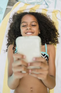 Smiling Hispanic girl texting on cell phone at swimming pool