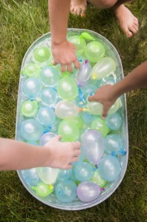 Hands of girls reach for water balloons in tub