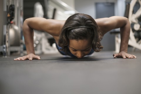 Mixed Race woman doing push-up on floor at gymnasium