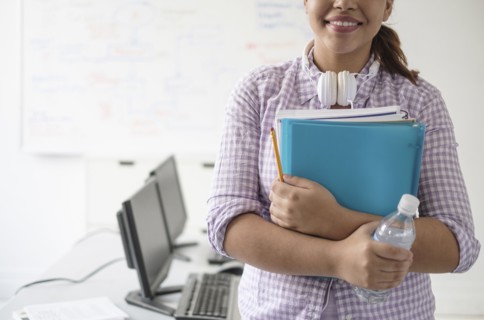 Smiling Hispanic woman holding books and water bottle in computer lab