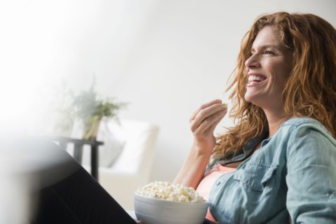 Laughing Caucasian woman eating bowl of popcorn