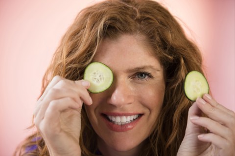 Smiling Caucasian woman covering eye with cucumber slice