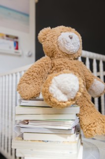 Teddy bear on stack of books near crib