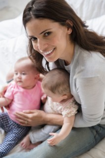 Caucasian mother sitting on bed holding twin baby daughters