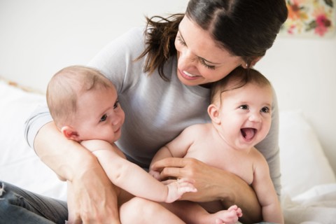 Caucasian mother holding twin baby daughters in lap on bed