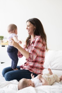 Caucasian mother playing on bed with twin baby daughters