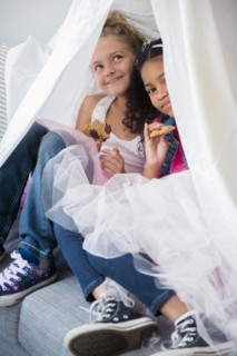 Girls wearing tutus in blanket fort on sofa