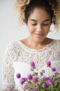 Mixed Race woman wearing wedding dress admiring bouquet