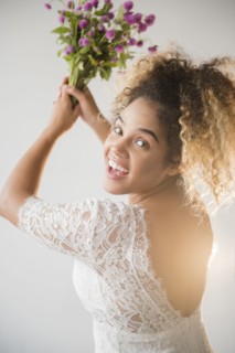 Mixed Race woman wearing wedding dress tossing bouquet