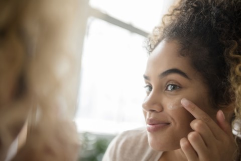 Mixed Race woman applying lotion to cheek