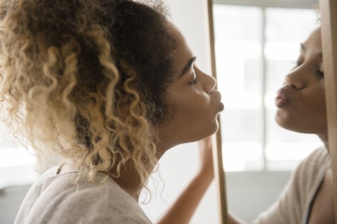 Mixed Race woman puckering lips in mirror