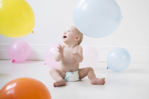 Caucasian baby boy sitting on floor watching balloons