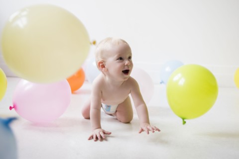Caucasian baby boy crawling on floor watching balloons