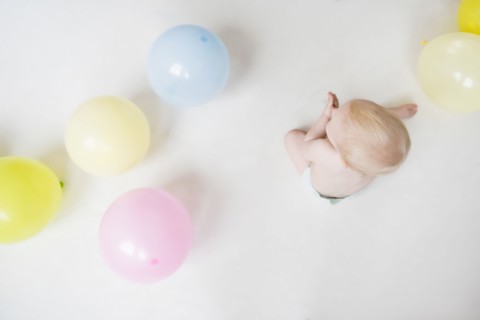Caucasian baby boy sitting on floor with balloons