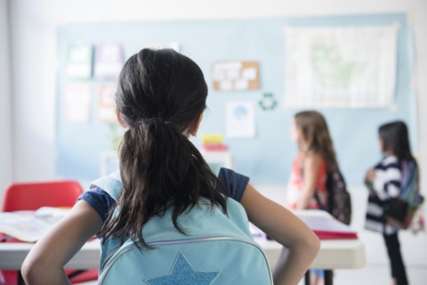 Girl in classroom wearing backpack watching classmates