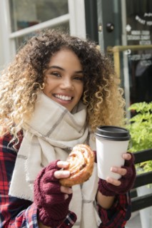 Smiling Mixed Race woman showing donut and coffee cup