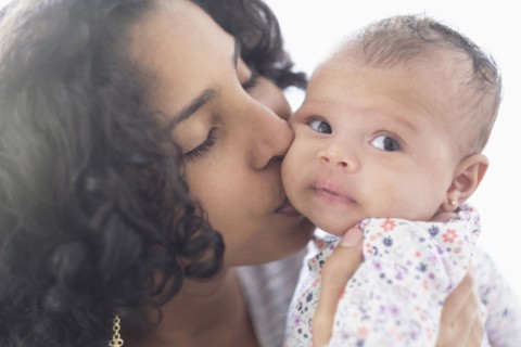 Hispanic mother kissing baby daughter on cheek