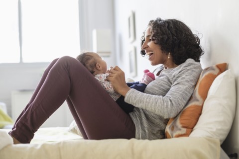Hispanic mother playing with baby daughter on bed