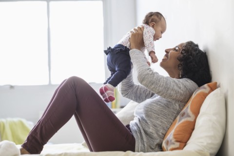 Hispanic mother playing with baby daughter on bed